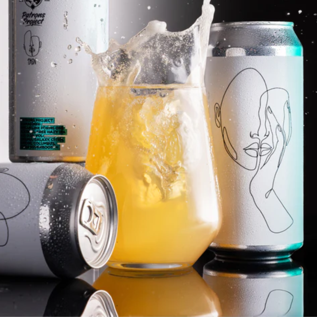 Cans of a beverage with a glass of yellow liquid and ice cubes on a reflective surface.