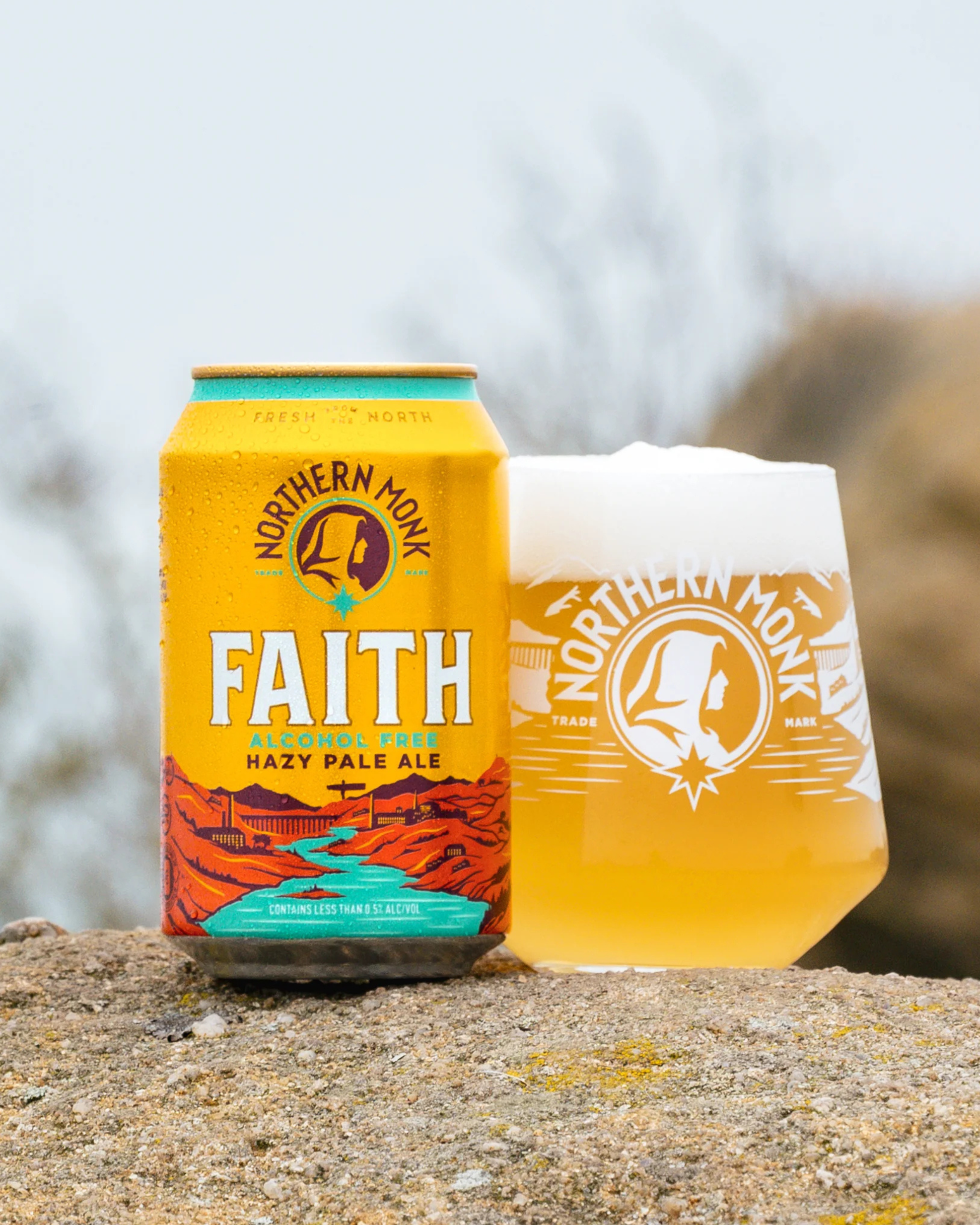 Northern Monk Faith Alcohol Free beer can and glass of the beer on a stone surface with a blurred natural background
